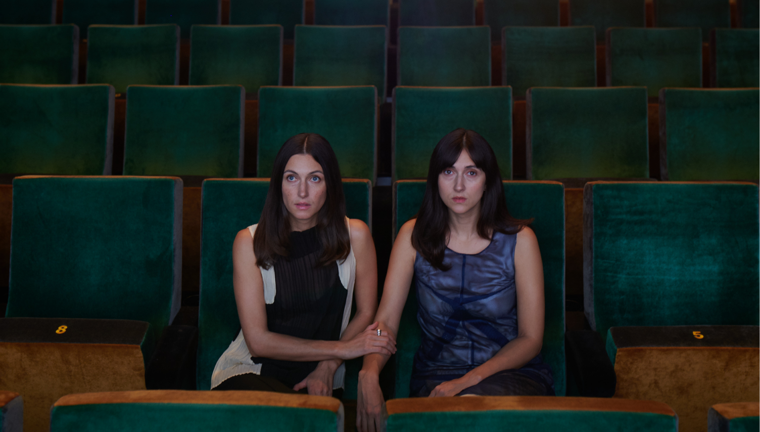 Flo and Kim Nüesch seated together in the middle of an empty theatre auditorium, surrounded by rows of green velvet seats.
