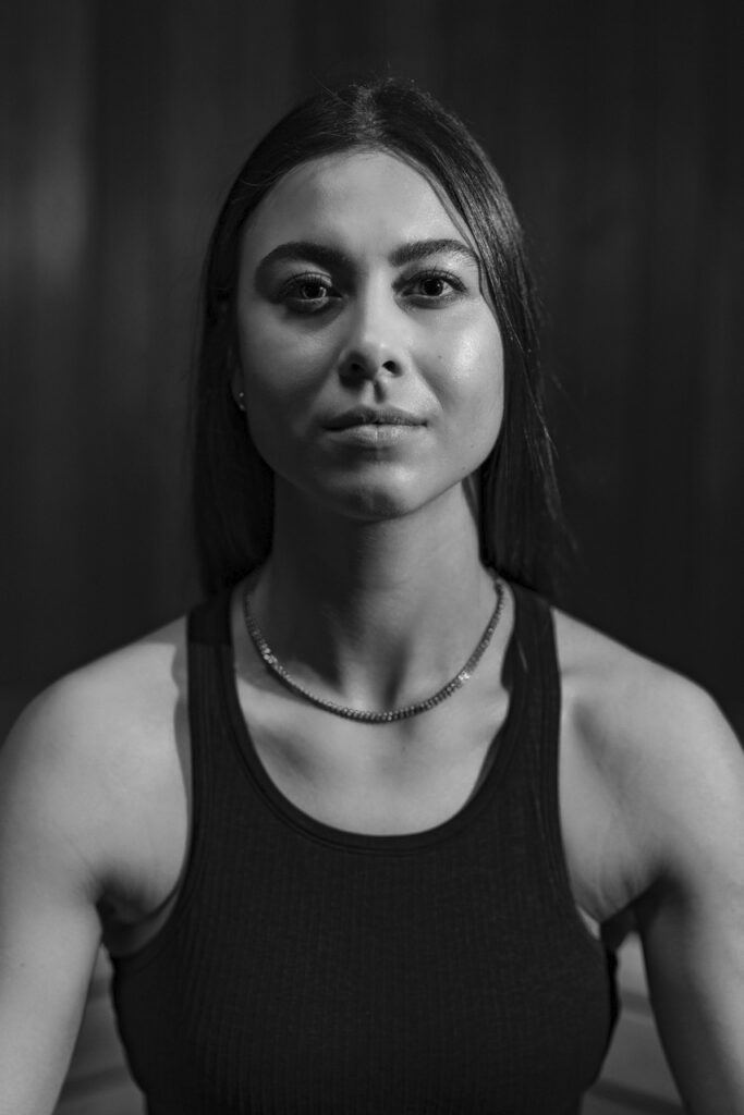 Young woman wearing a black sleeveless top, looking directly into the camera.