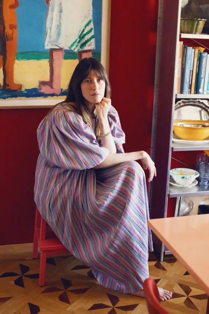 Anouck Mutsaerts sitting in a colourful interior, wearing a striped dress.