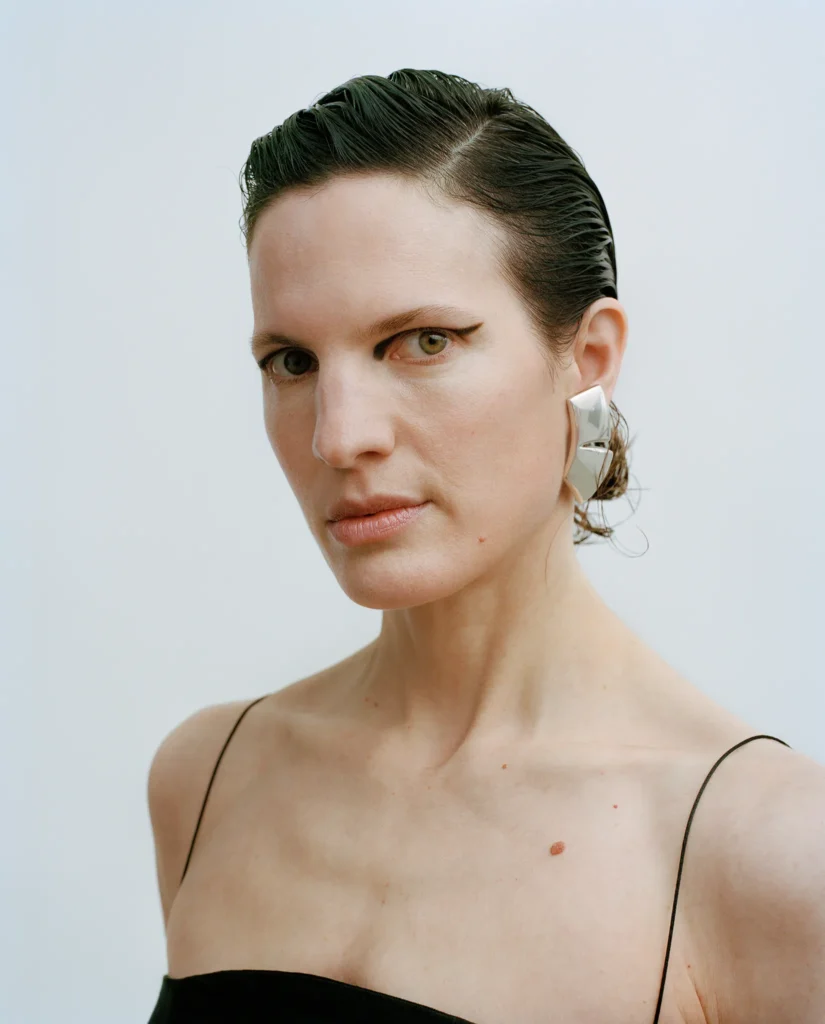 Portrait of Annina with slicked-back dark hair, graphic black eyeliner and a black camisole.