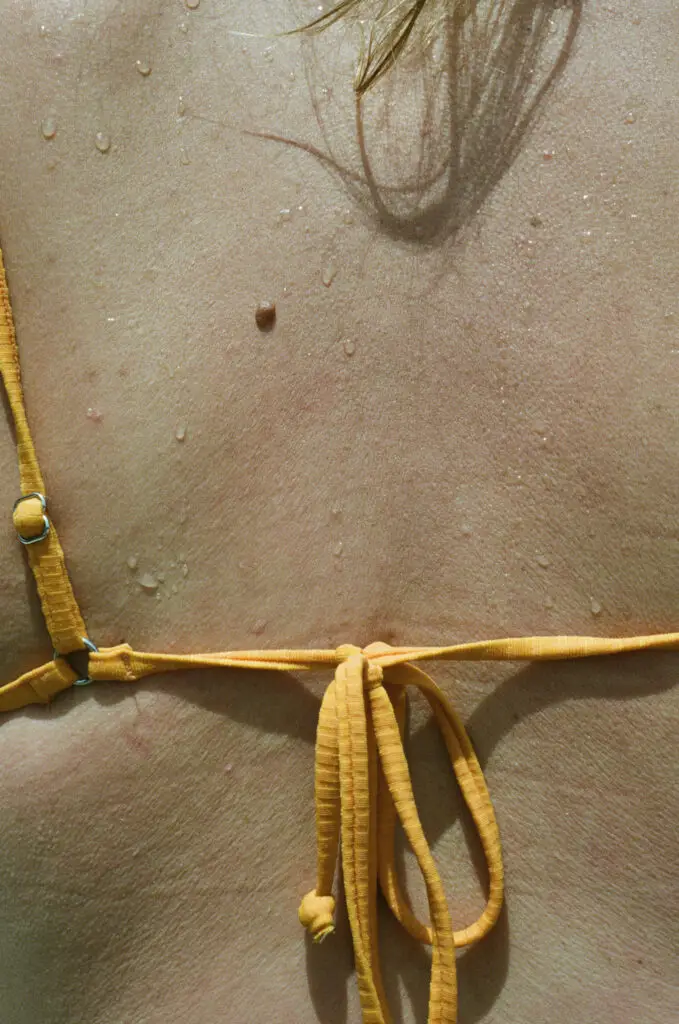 Back view of a woman in a bikini top with beads of sweat visible on her skin in the summer heat.