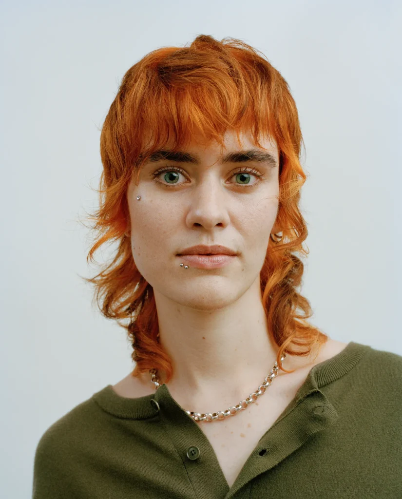 Portrait of Iris with a braided updo, turquoise eye makeup and a pale blue sleeveless top.