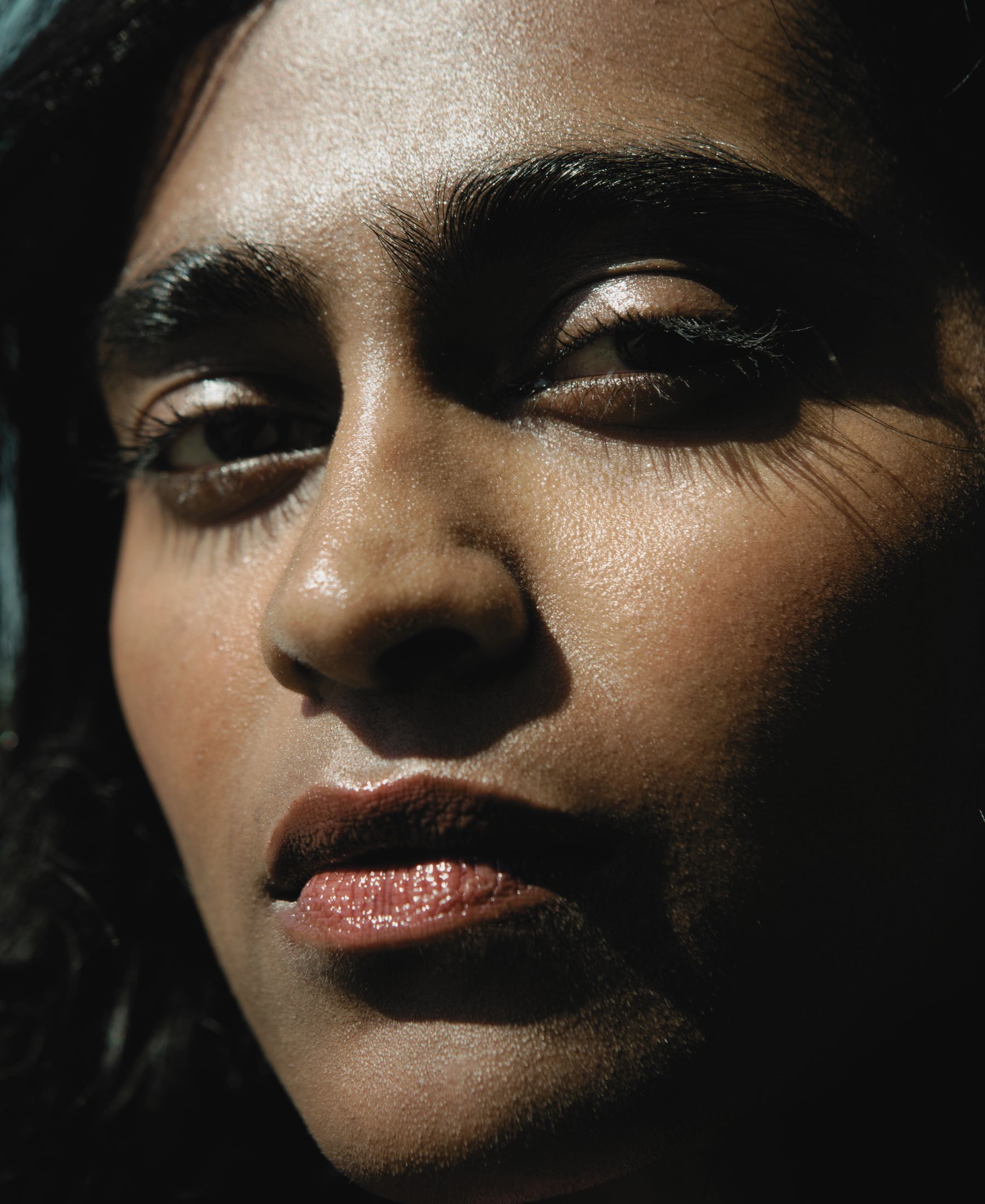 Barathy Akkan in close-up, with hard sunlight cutting across her face and deep shadow defining the portrait.