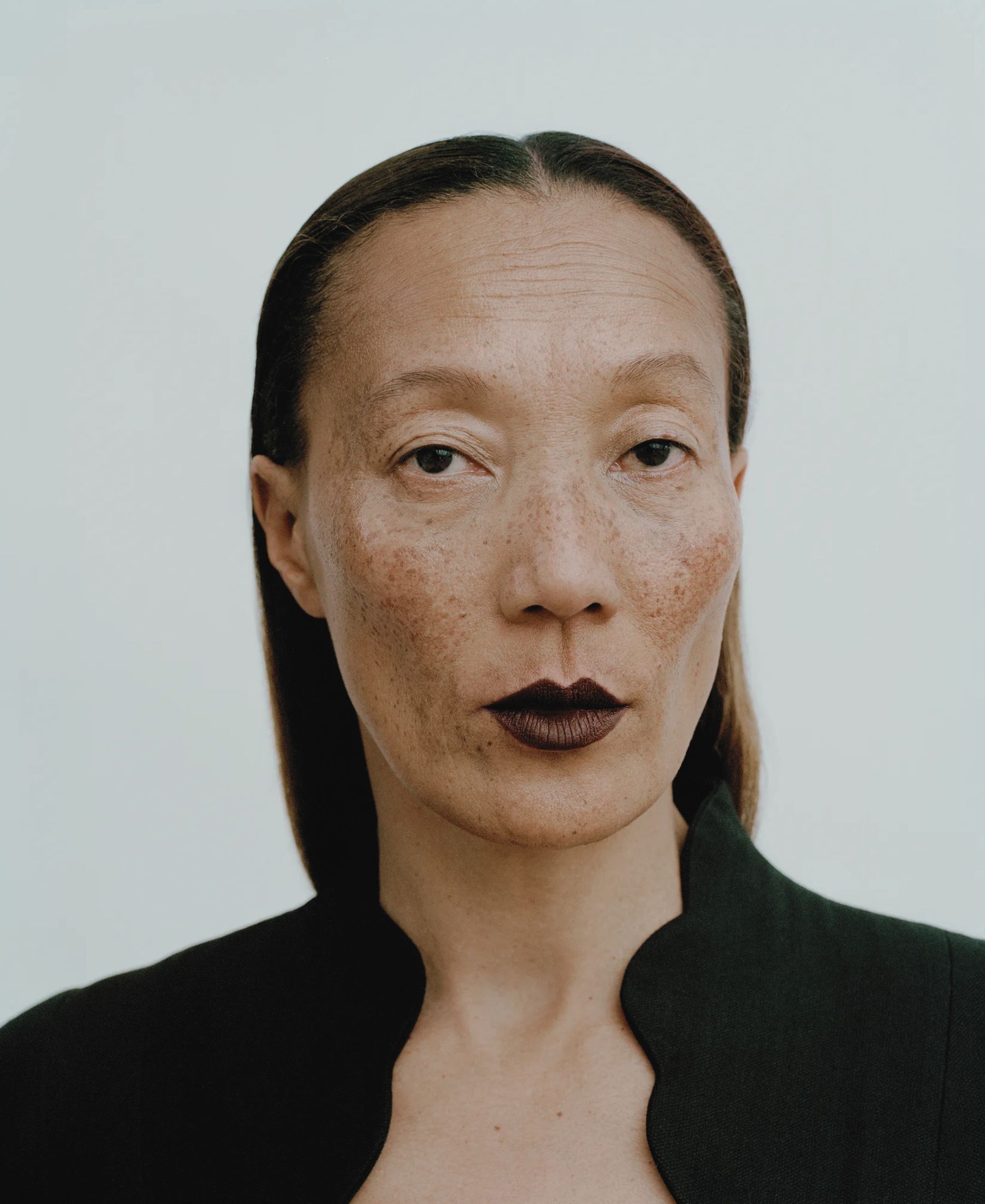 Kojolee facing the camera in deep burgundy lipstick and a structured black vintage blazer.