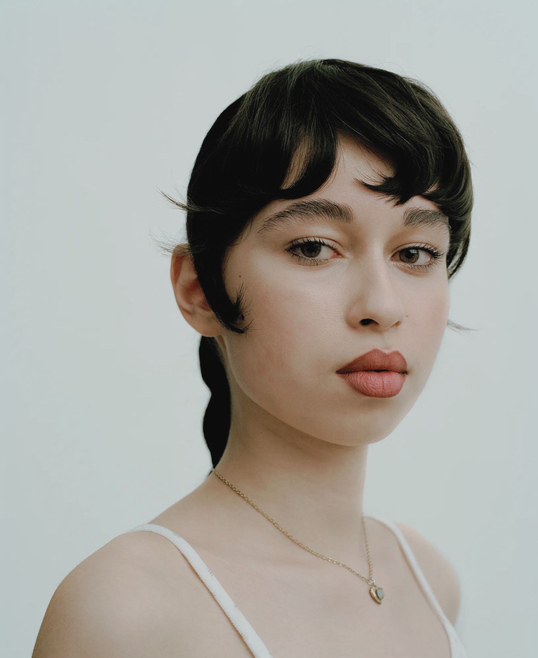 Jasmina in close-up, with sculpted black hair, softly defined lips and a fine gold necklace.