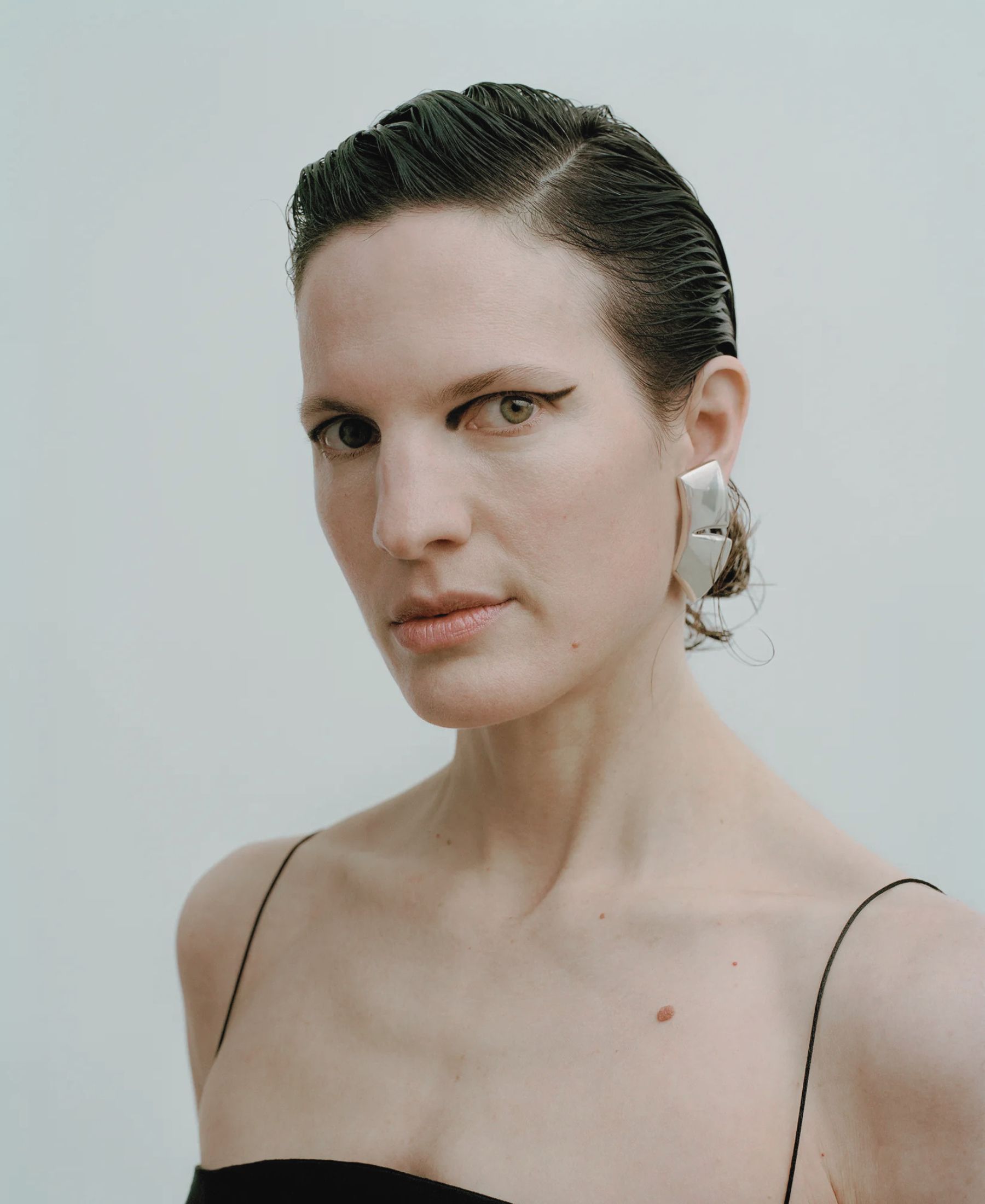 Annina in close-up, with slicked-back hair, graphic black eyeliner and oversized silver earrings.