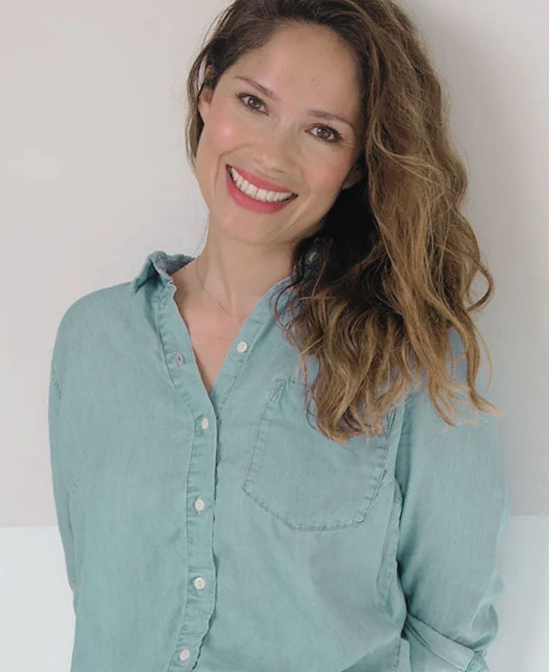 Lina Hanson smiling in a pale blue shirt, with long softly waved hair falling over one shoulder.