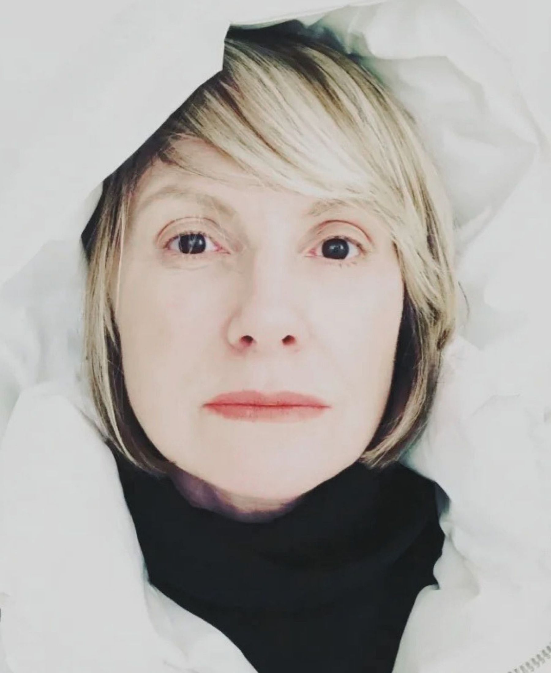 Close portrait of Kelley Ralph with a short blonde bob, framed by pale outerwear over a black high-neck top.