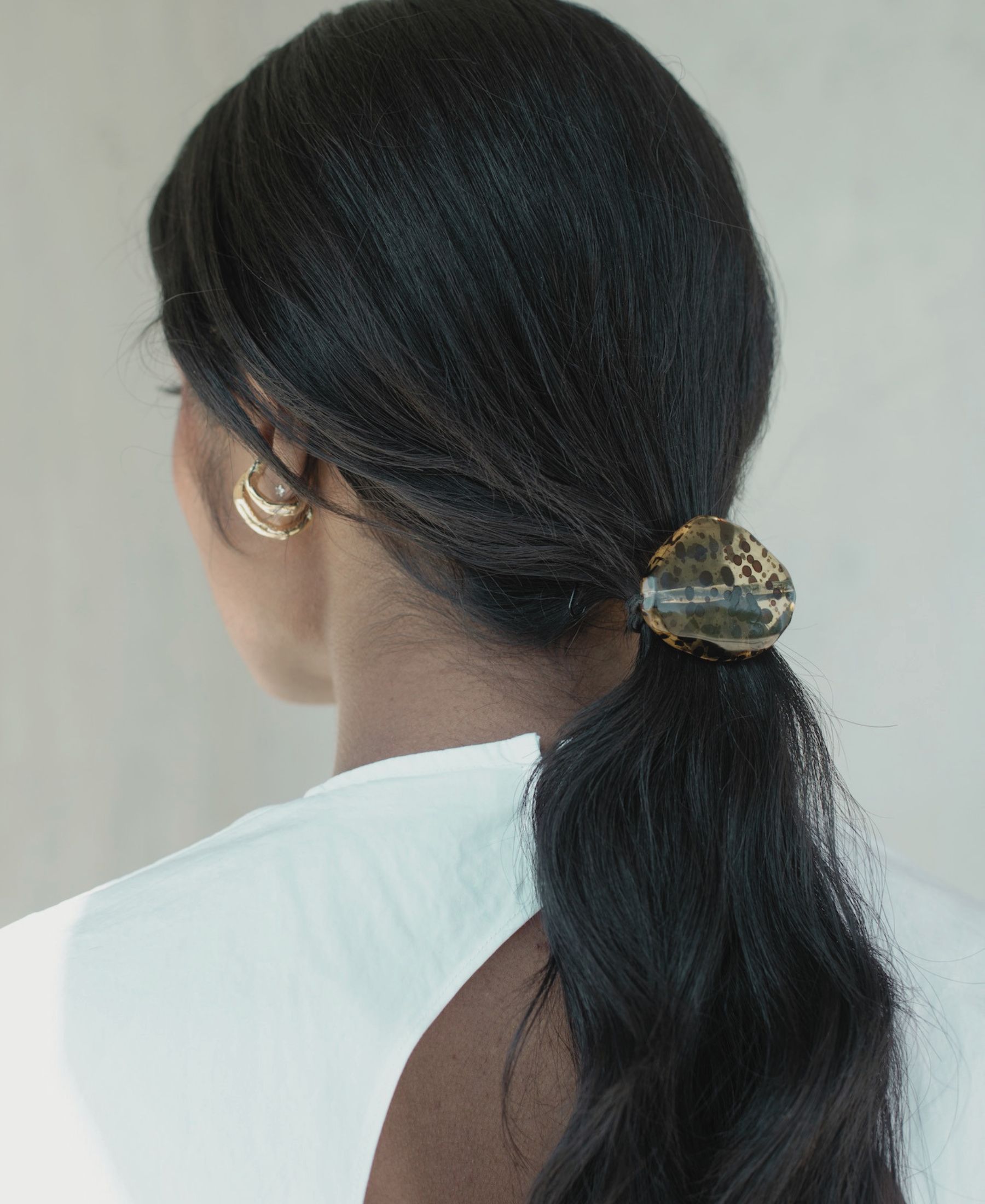 Back view of Barathy Akkan’s low ponytail, secured with a sculptural hair accessory and framed by gold earrings.