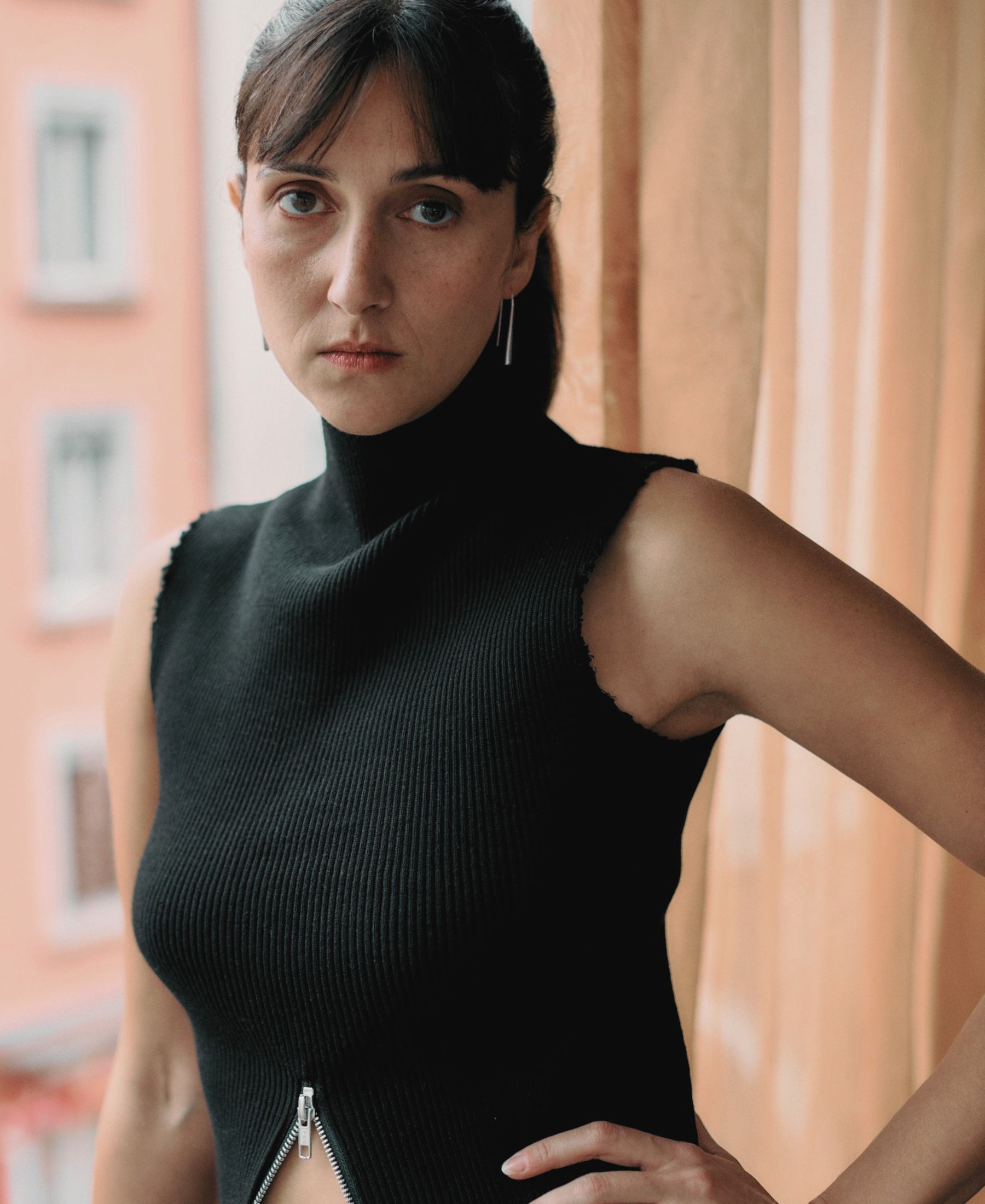 Portrait of one of the Nüesch Sisters in a black sleeveless top, standing beside a window in soft daylight.