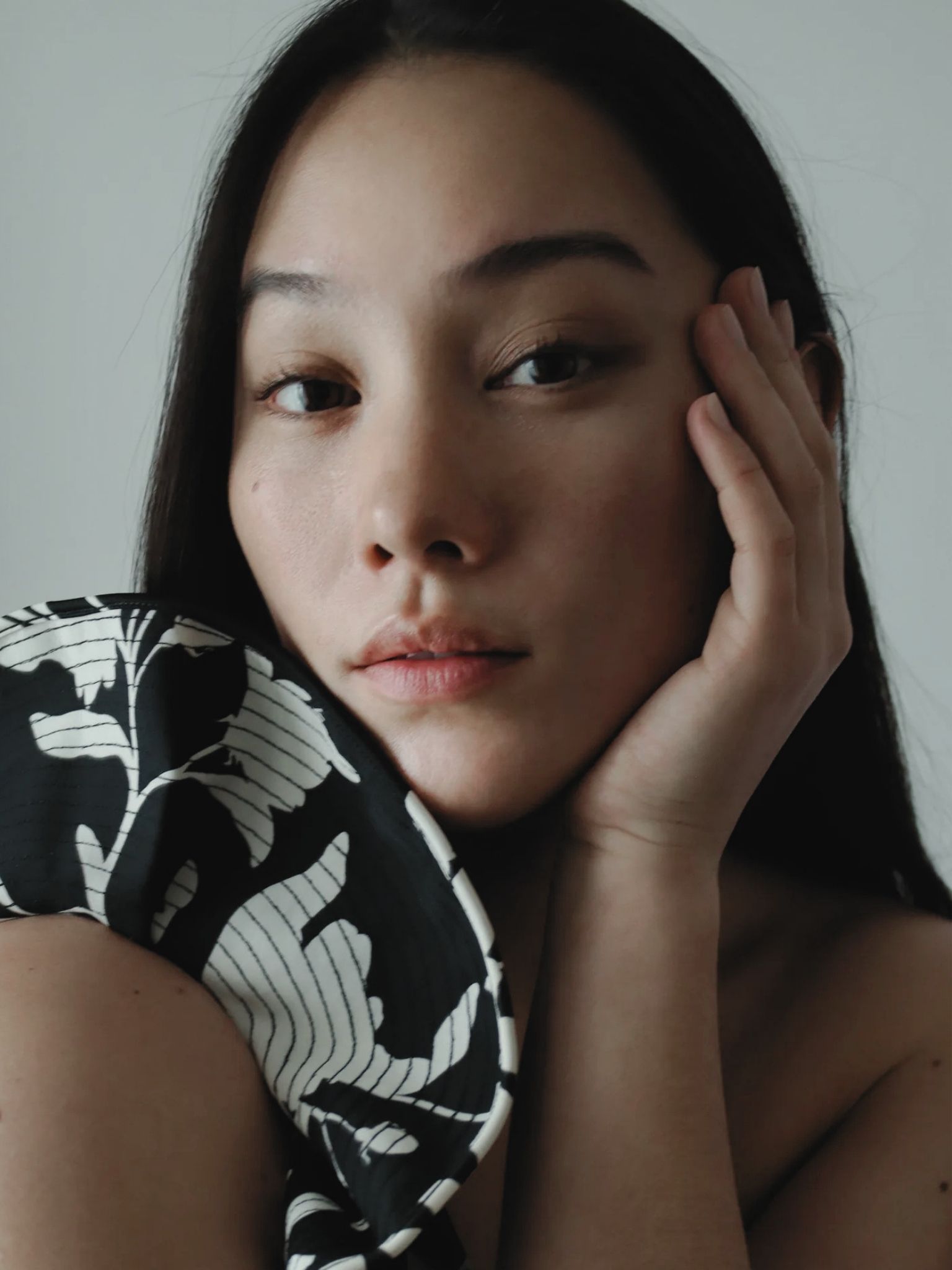 Close portrait of Momo Tanner with long dark hair, resting her face against one hand beside black-and-white patterned fabric.