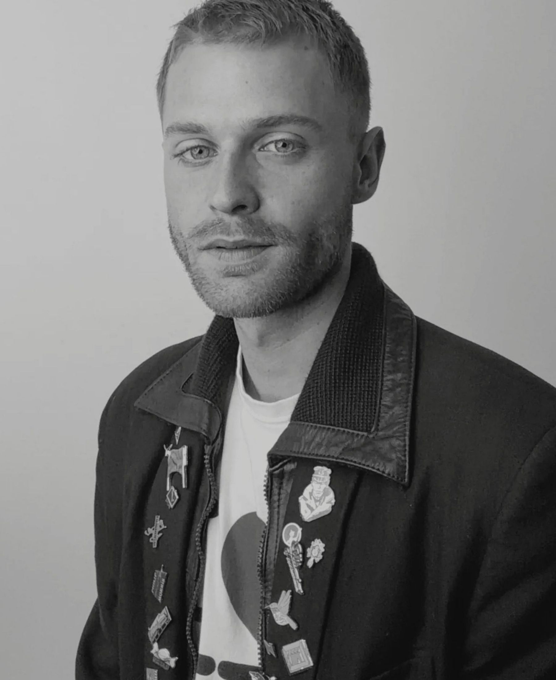 Black-and-white portrait of Elay Neal Moses with closely cropped hair, wearing a dark jacket detailed with small pins.