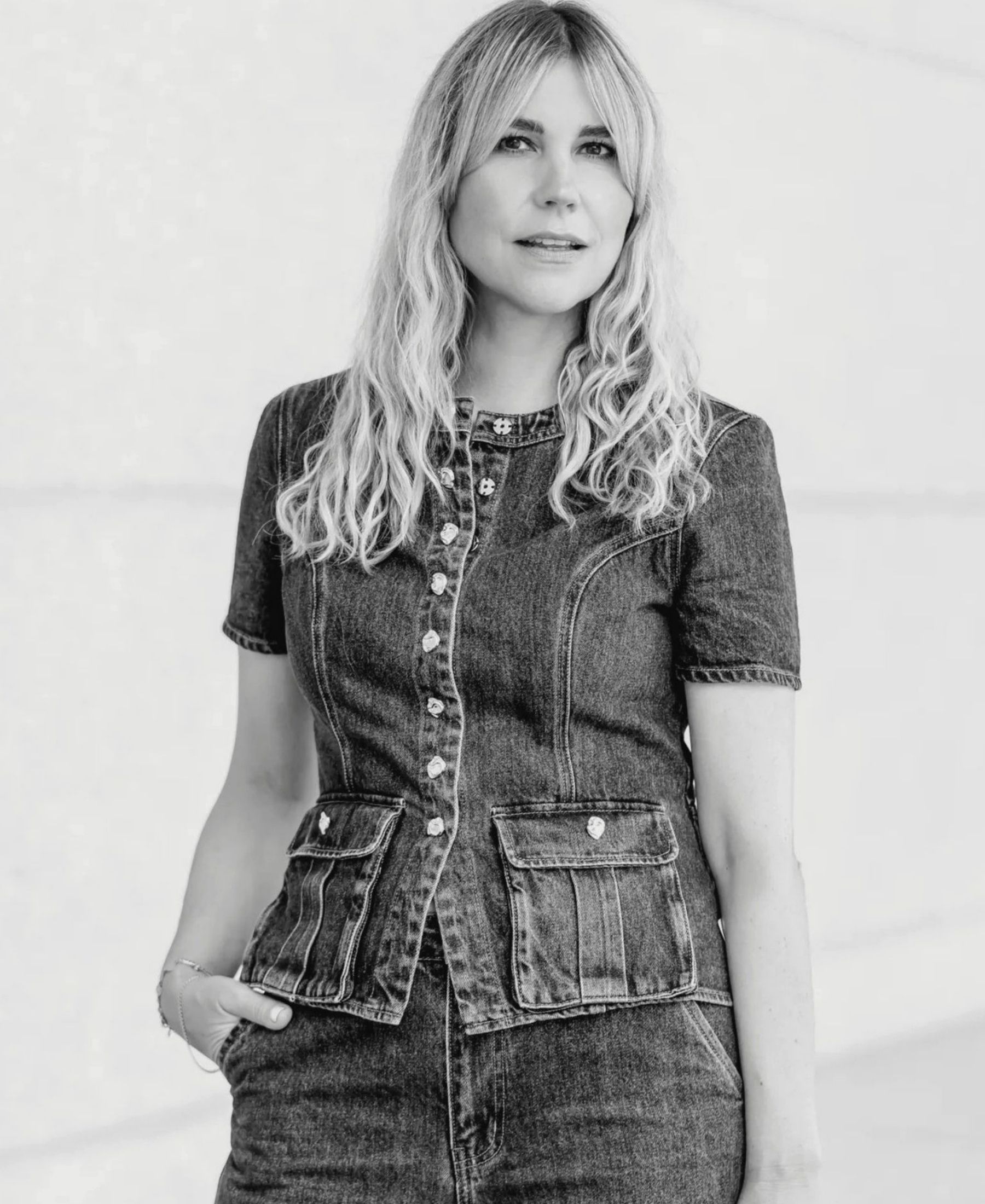 Black-and-white portrait of Stephanie Neubert with long wavy blonde hair, wearing a fitted dark denim dress.