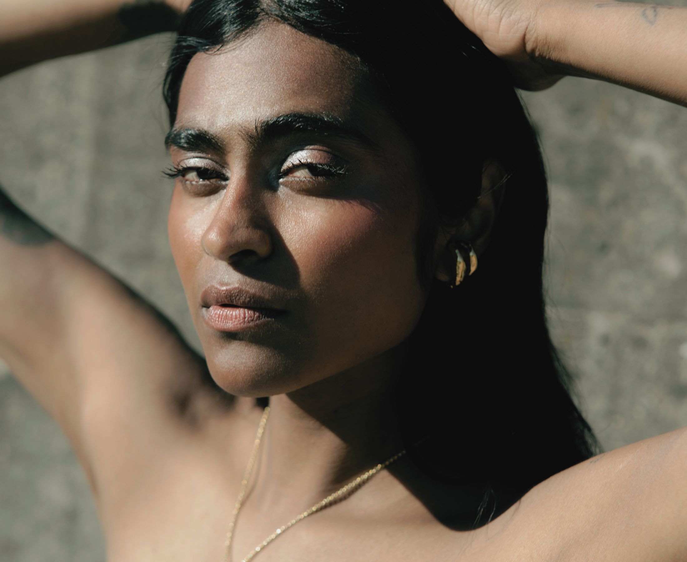 Barathy Akkan reclining in sunlight, wearing gold jewellery with her hair swept back from her face.