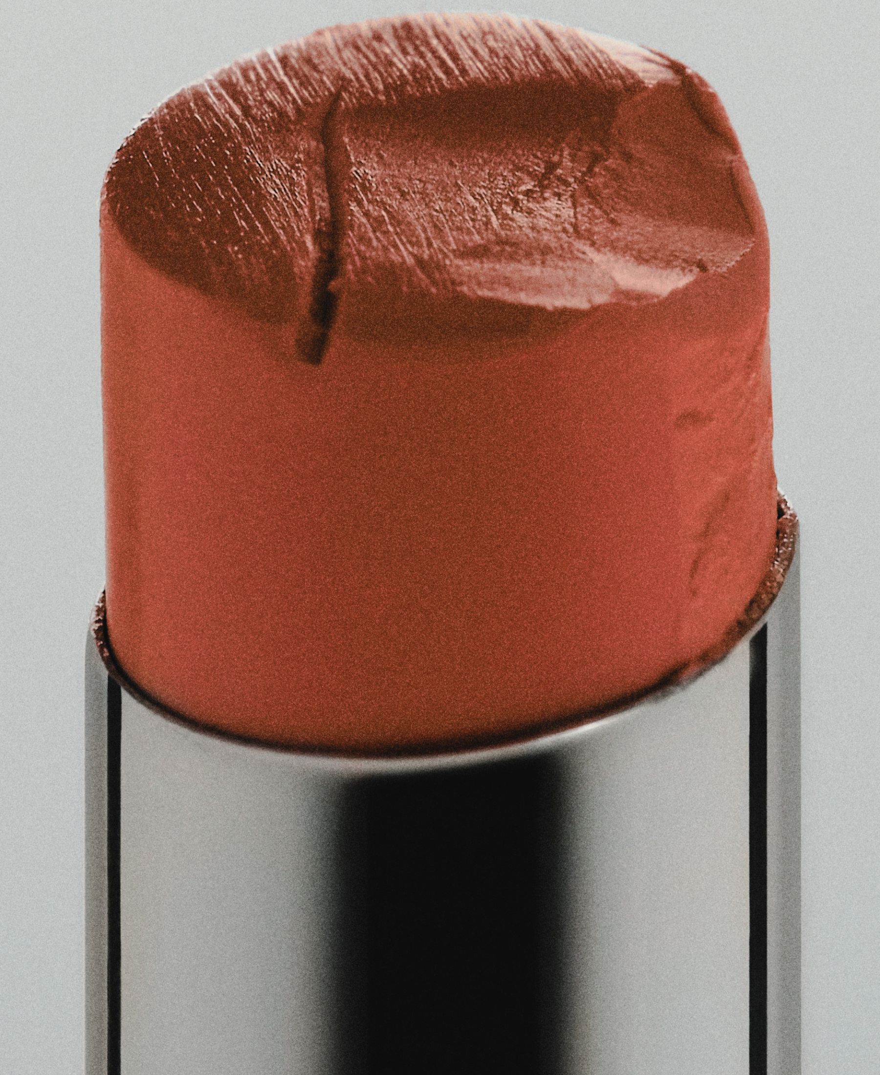 Extreme close-up of a warm rose lipstick with its textured surface visible above a silver case.