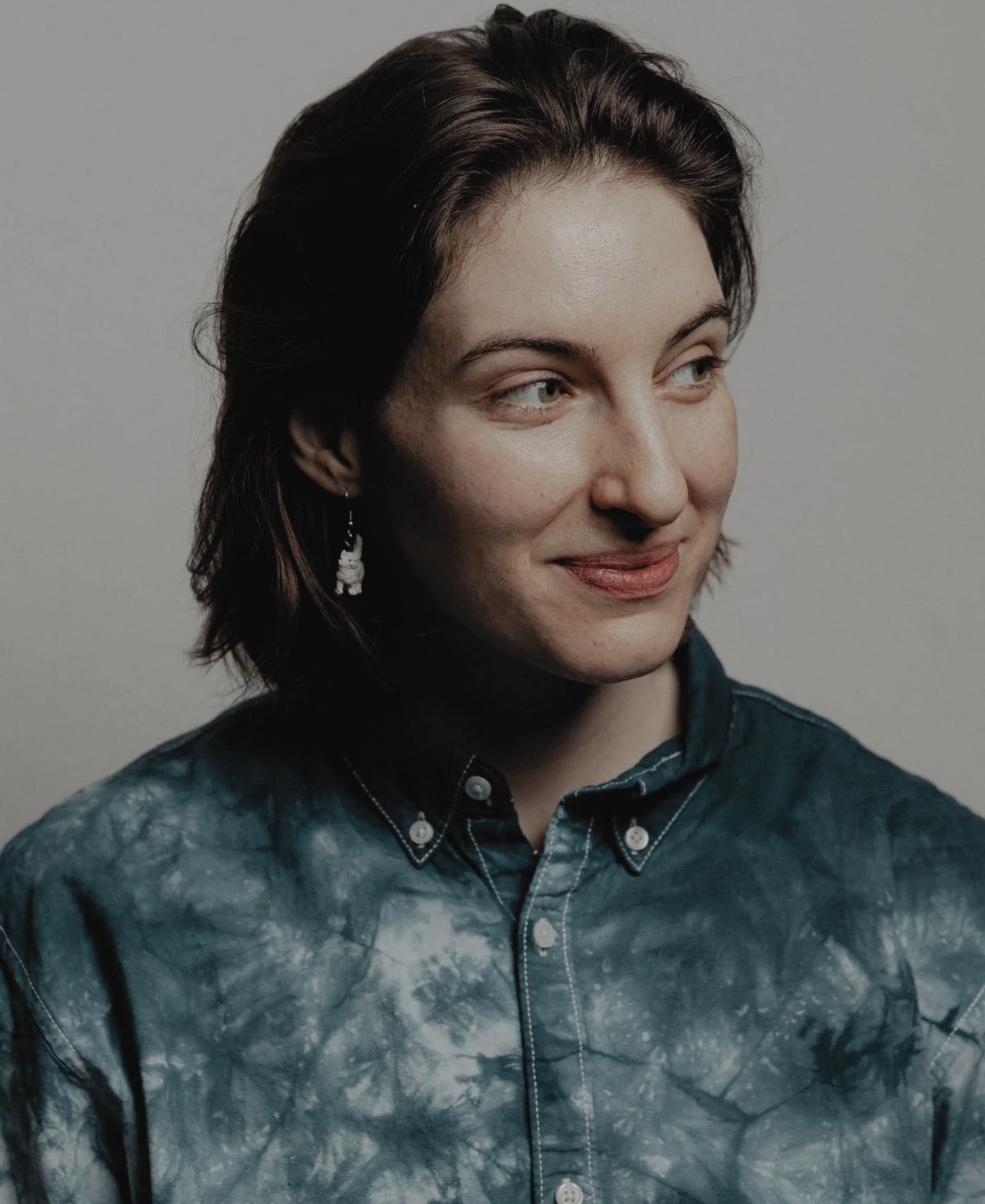 Portrait of Anna Rosenwasser with short dark hair, wearing a blue marbled shirt and looking away from the camera.
