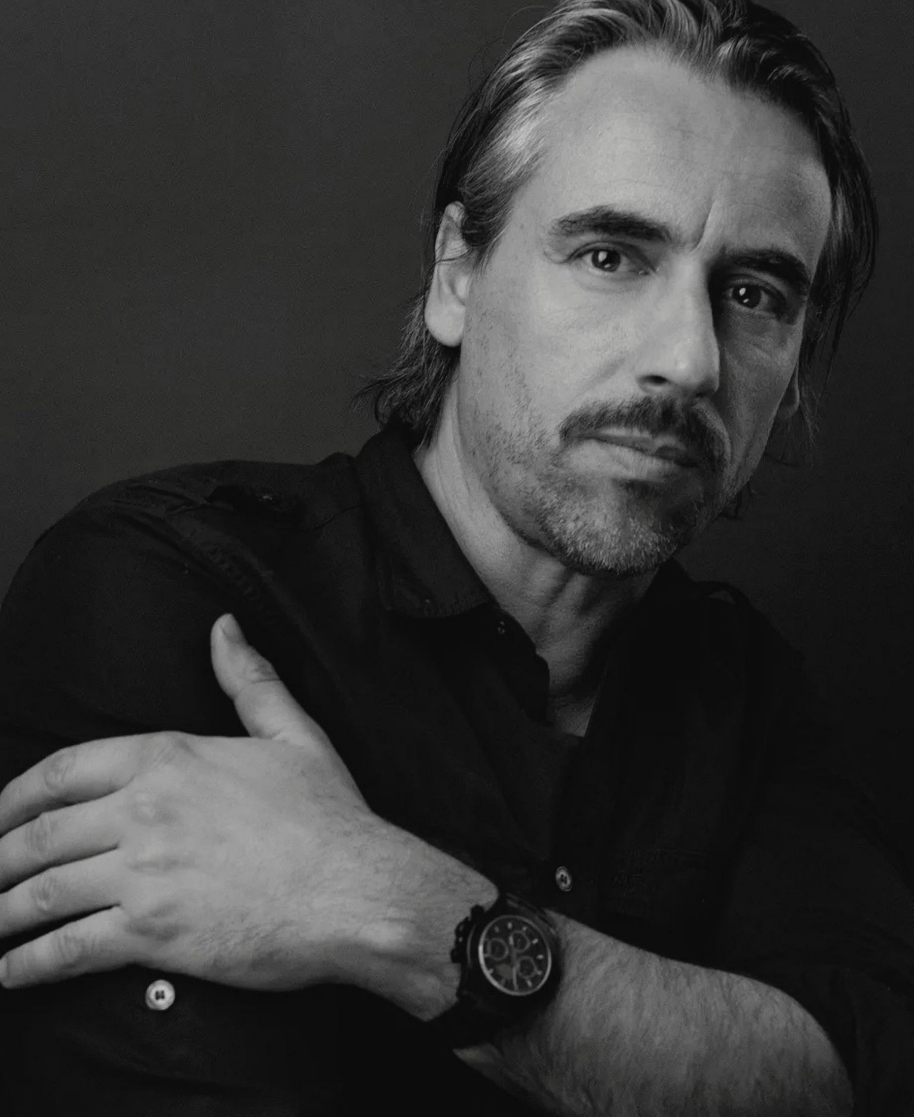 Black-and-white close portrait of Charles Blunier in a dark shirt, his arm folded across his chest and a watch at his wrist.