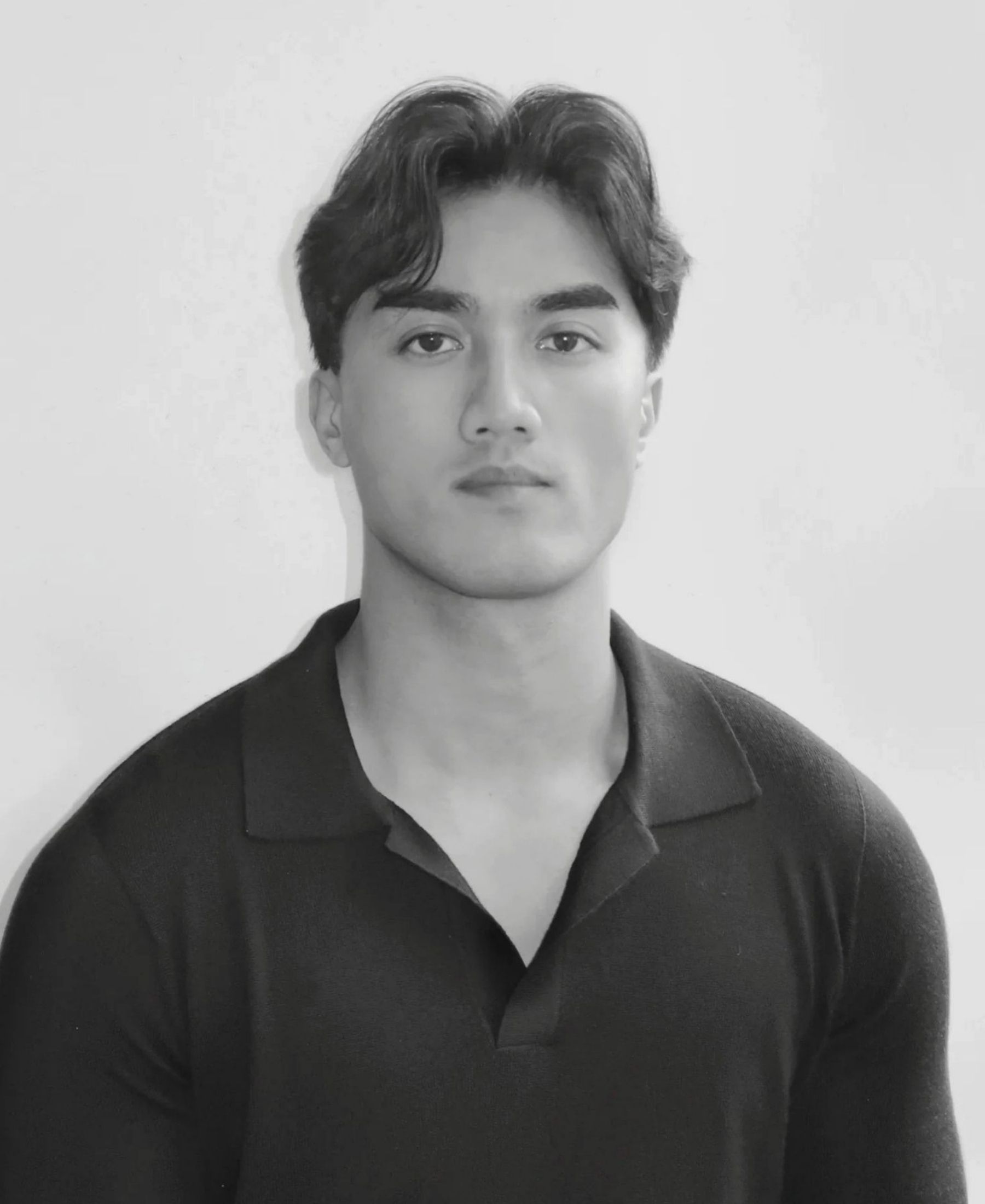 Black-and-white portrait of At Hergett with short dark hair, wearing a simple black polo shirt against a pale background.