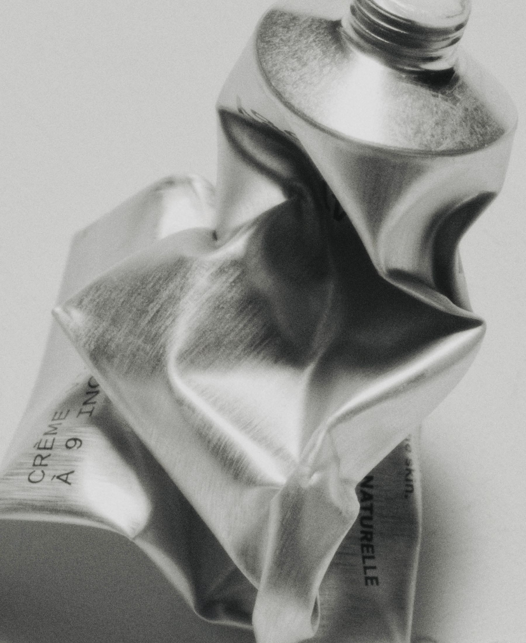 Black-and-white still life of a crumpled silver tube of Typology face moisturizer.