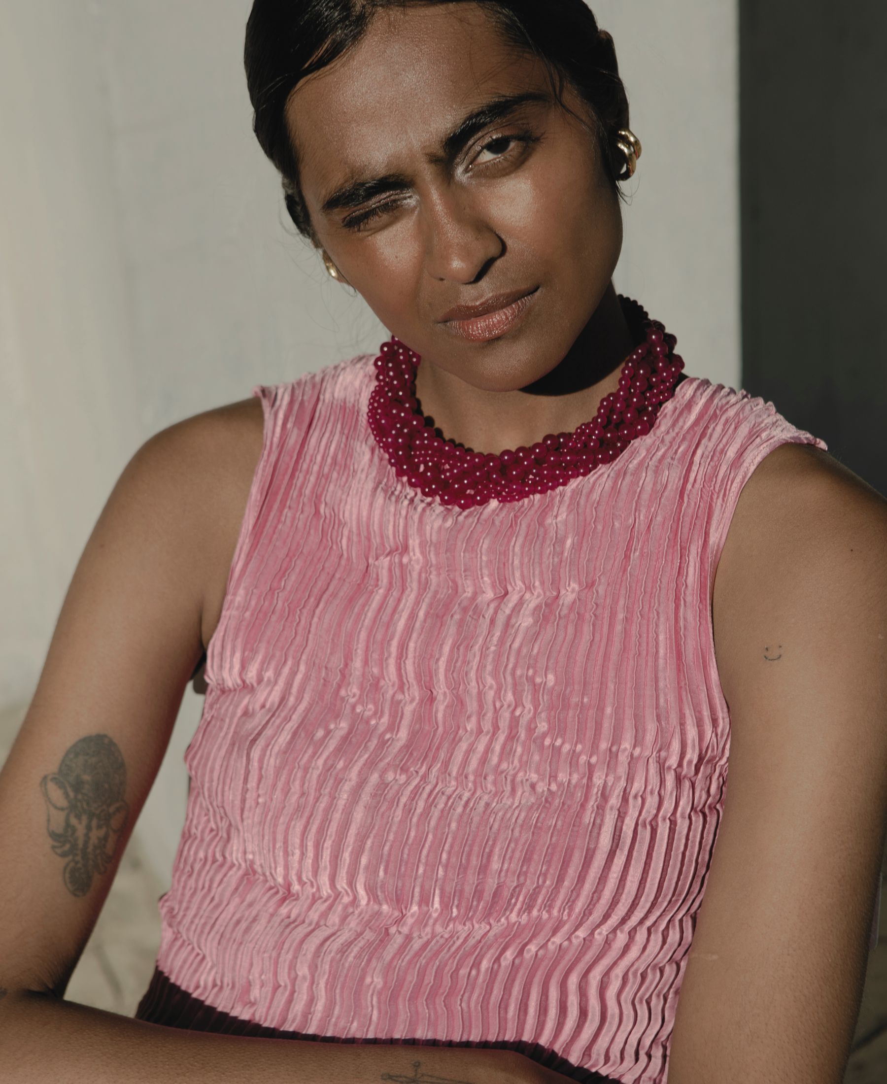 Barathy Akkan in a pleated pink dress, wearing a deep-red beaded necklace in direct sunlight.