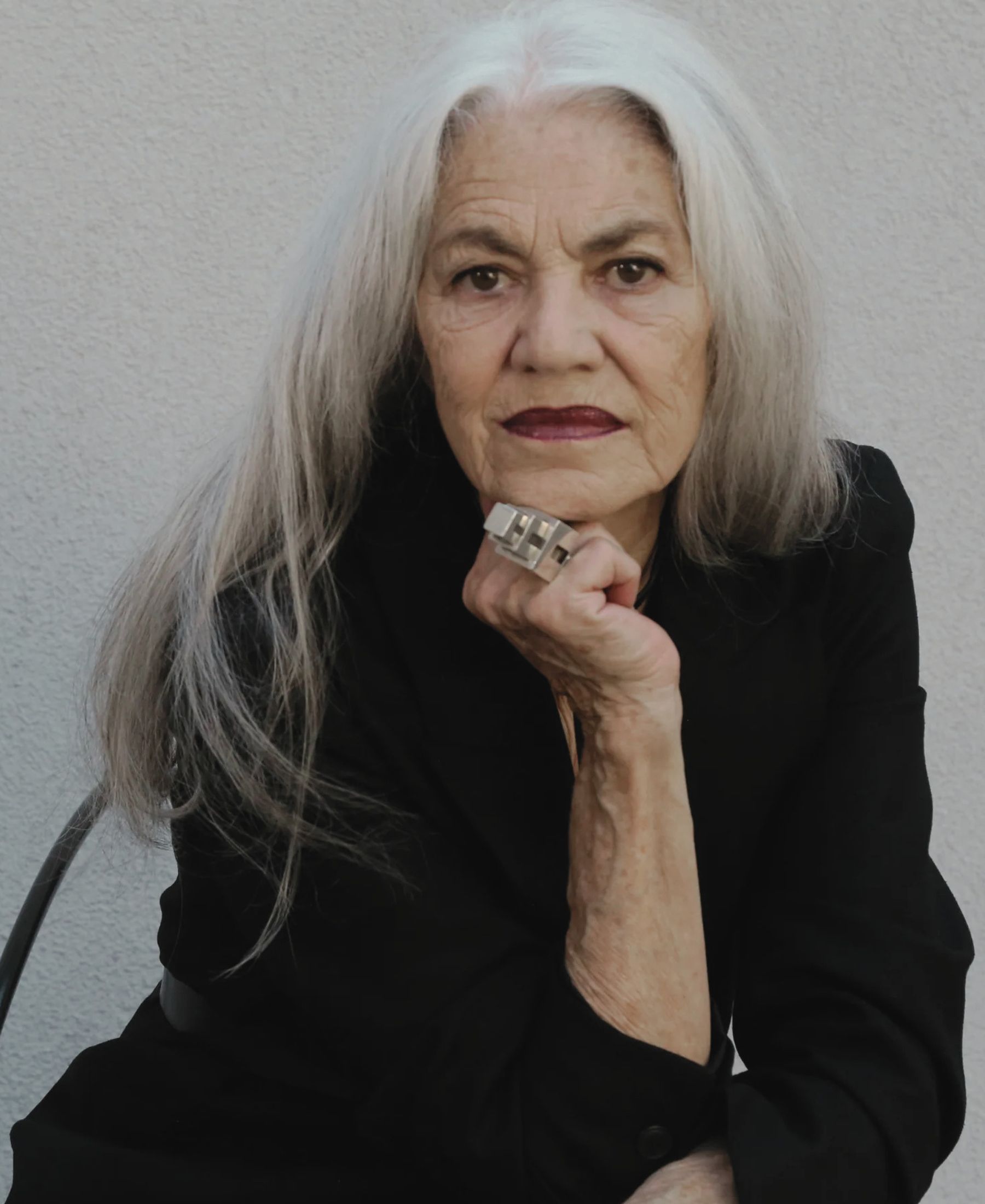 Portrait of Carmen Meier-Meister with long silver hair, dressed in black and resting her chin on one hand.