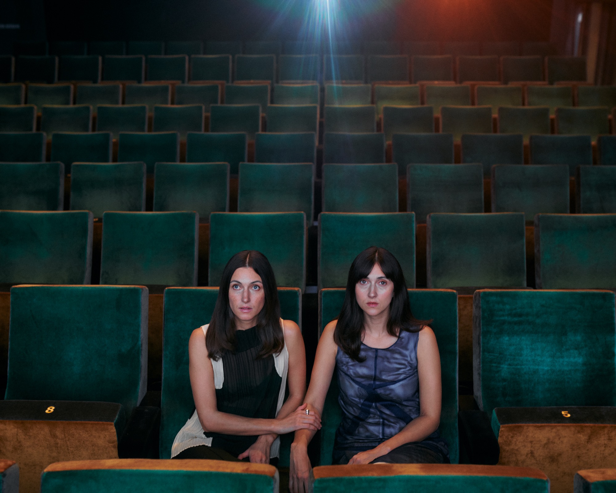 Florine and Kim Nüesch seated together among rows of green cinema seats, facing the camera beneath the projection light.